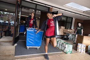 Two students in volleyball shirts wheel a cart outside Fritz-Conrad
