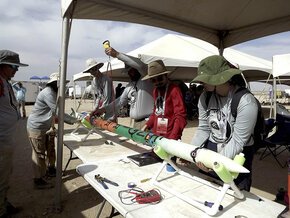 Team members under tent lift rocket for transport to launchpad