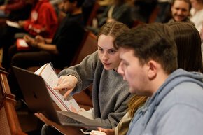 Two students compare written and laptop notes in the audience at an event