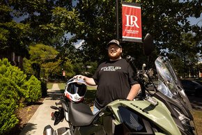 Kevin Miller stands under an LR banner on the quad with his motorcycle