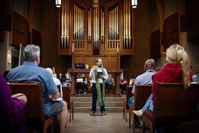 Pastor Vern talks to a congregation in front of the organ in Grace Chapel