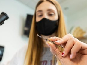 Biology student Olivia Nunn holds an ant in tweezers next to a microscope.