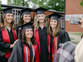 Five graduates in regalia pose and smile for the camera