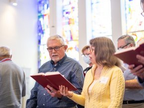 Alumni stand in chapel and read from the hymnal