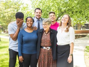 A group of six people smile and laugh while outside