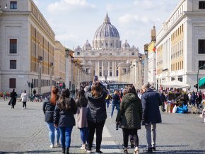 A group of students walk away from the camera toward historic buildings in Italy