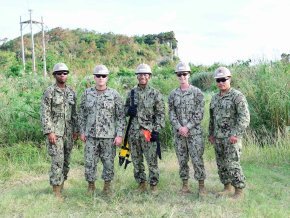 Five men in U.S. Navy fatigues stand together outside