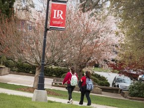 Students walk under an LR banner on a signpost with blooming trees in the background