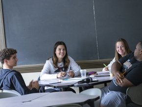 Four students study together around a table in front of a chalkboard