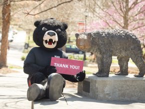 Joe Bear sitting next to The Cub statue holding a red sign that reads "Thank you!"