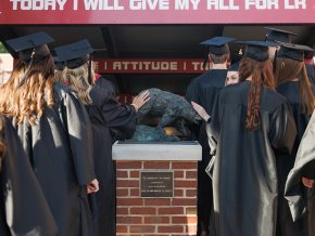Processional of graduates in robes pause to touch the model of the Charge as they enter Moretz stadium for commencement