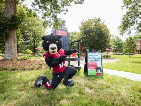 Joe Bear poses in front of the Bear Grove Big Chair and a welcome sign