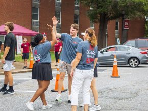 Move-in crew of four people high-five in parking lot outside Fritz-Conrad