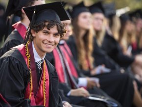 Student in audience smiles to camera while attending commencement ceremony