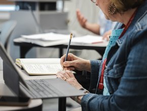 A graduate student takes notes next to a laptop in front of her