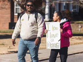 A man and a woman marching on MLK Day 2025, one carries a sign reading "I too have a dream."