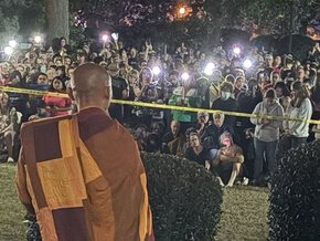 Back view of a Buddhist monk facing a crowd and lights from the steps of Beam Hall in Columbia