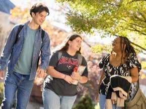 Three students talking while walking across campus