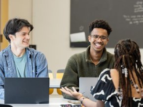 Three students sitting at a table talking in classroom
