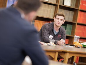 A student in front of a wall of books at a seminar table 