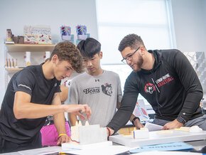 Three men work together assembling a project in a lab