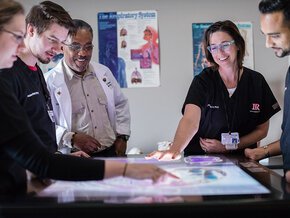 Professors and PA studies students gather around a light table to look at imaging