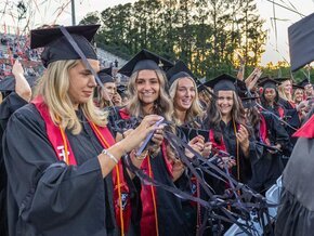 Red and black streamers fly over smiling graduates on stadium field