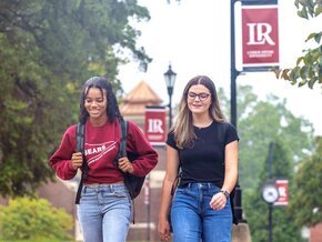 Two students walking on campus with LR banners in background