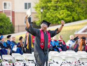 A student holds up his arms and his diploma at commencement