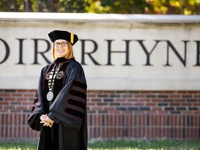 Summer McGee in academic regalia with the Lenoir Rhyne sign in the background