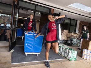 Two students in volleyball shirts wheel a cart outside Fritz-Conrad