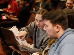 Two students compare written and laptop notes in the audience at an event