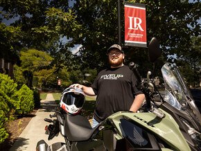 Kevin Miller stands under an LR banner on the quad with his motorcycle