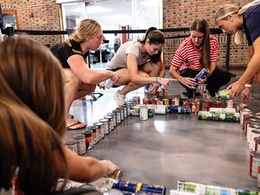 Womens lacrosse players surround stacks of cans in a rectangle