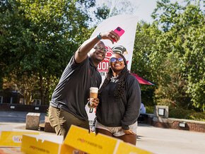 Harry Titus takes a selfie with a student in front of the Donuts with the Dean banner