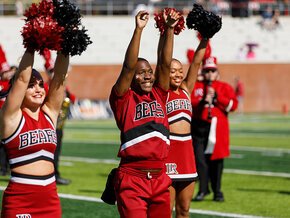 Four members of the spirit team raise their hands on the field
