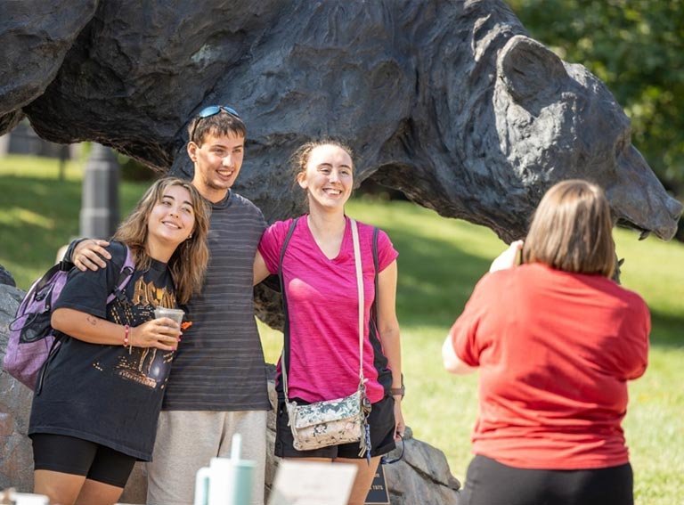 Students pose for photo in front of the Charge Bear statue on LR campus