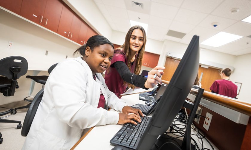 Two students review a computer screen in a simulated hospital station