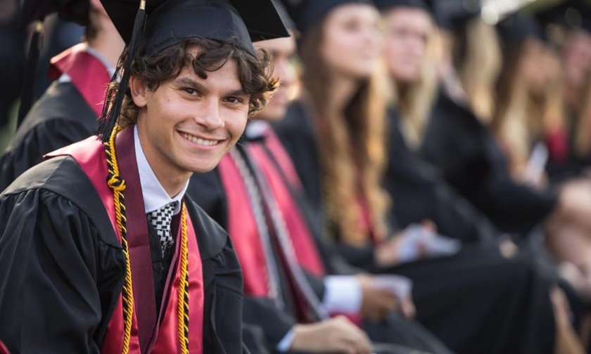 Student in audience smiles to camera while attending commencement ceremony