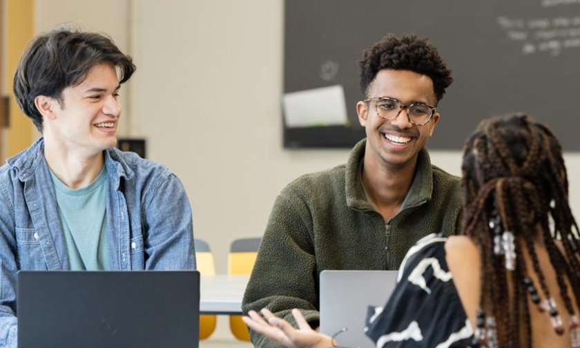 Three students sitting at a table talking in classroom