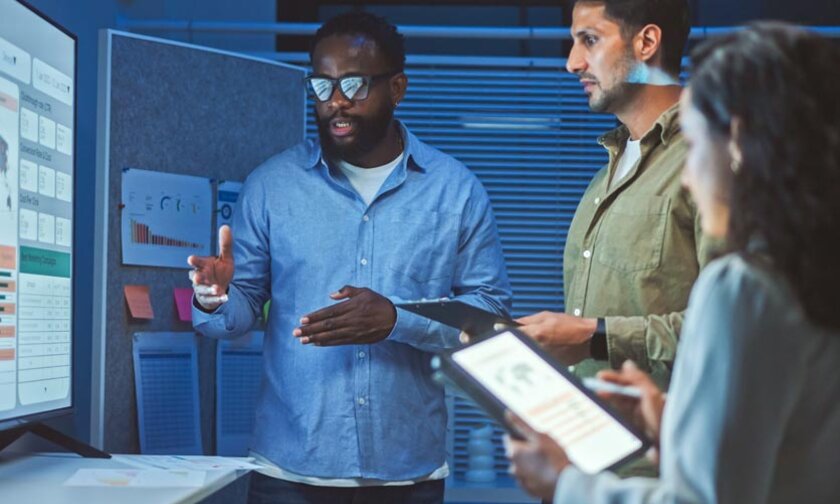 Three professionals discuss AI in front of data dashboard screen