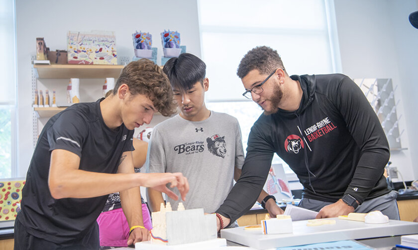 Three men work together assembling a project in a lab
