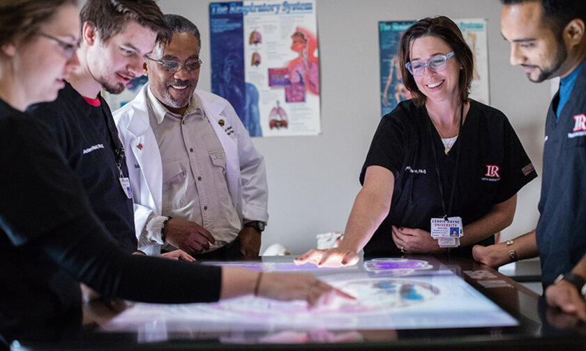 Professors and PA studies students gather around a light table to look at imaging