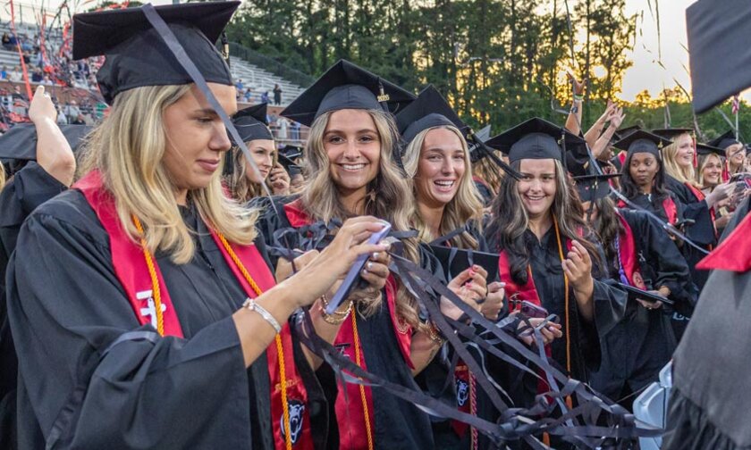 Red and black streamers fly over smiling graduates on stadium field