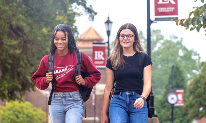 Two students walking on campus with LR banners in background