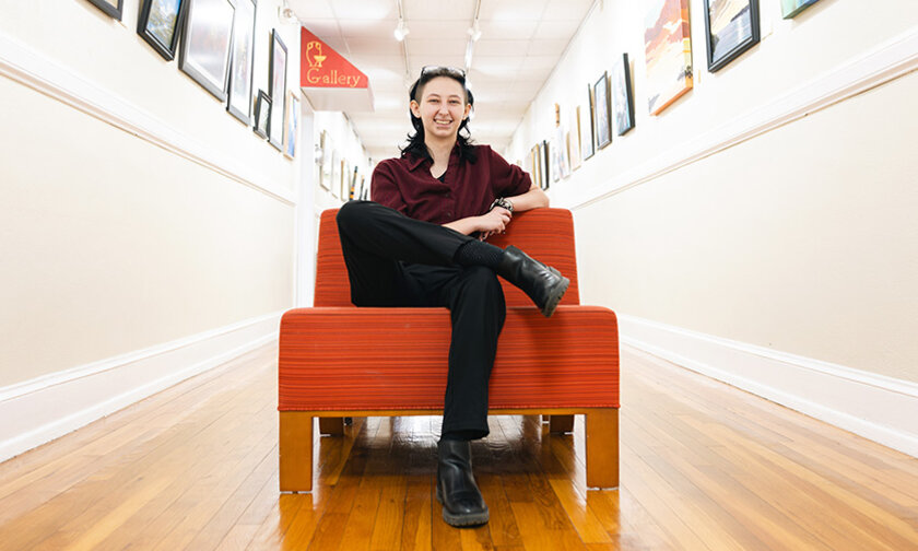 Ethan Craig sits in a red-orange chair in a hallway in the Mitford Museum
