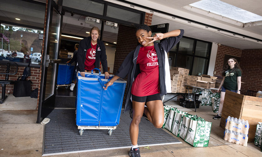 Two students in volleyball shirts wheel a cart outside Fritz-Conrad