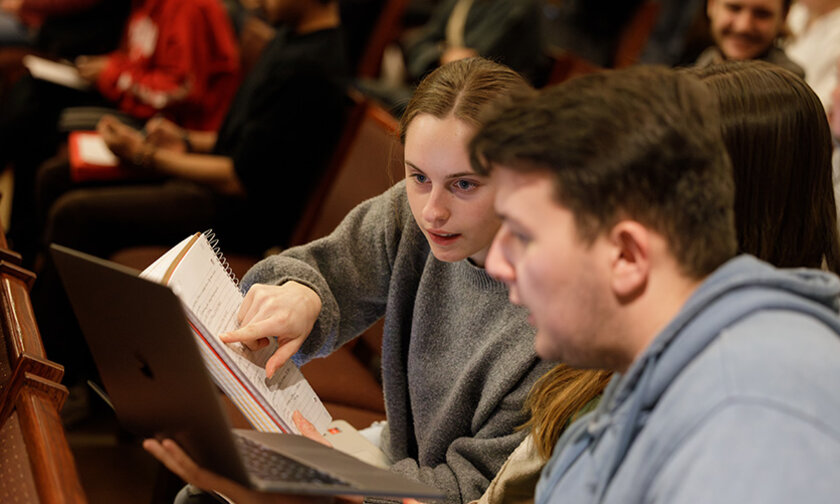 Two students compare written and laptop notes in the audience at an event
