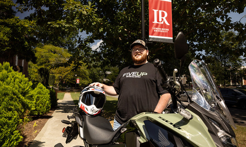 Kevin Miller stands under an LR banner on the quad with his motorcycle