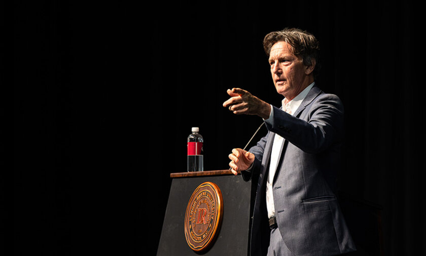 Andrew McCarthy leans on a podium with the LR seal on front
